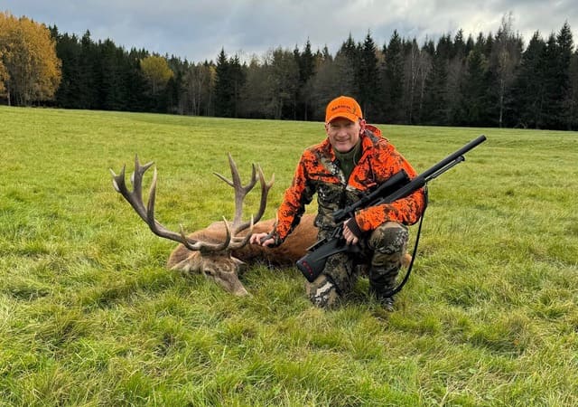 Anders Ek med felt 17-takkers kronhjort på gress, kledd i oransje jaktklær